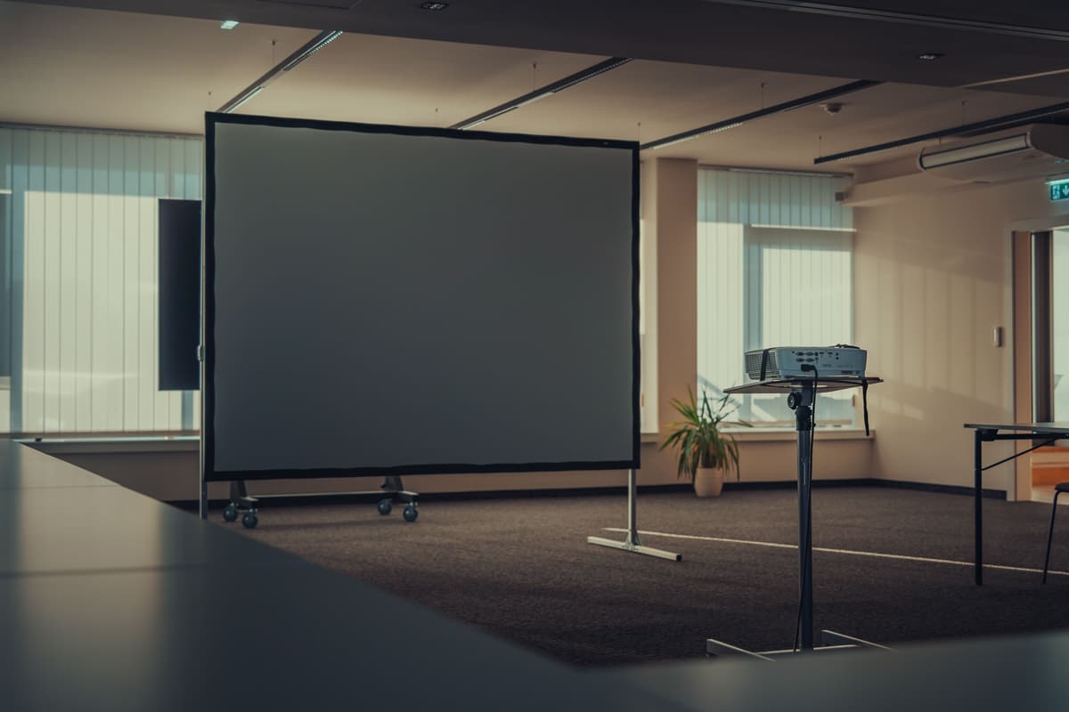 Leerer Besprechungsraum mit freistehender Leinwand im Rahmen und einem Projektor auf einem Stativ