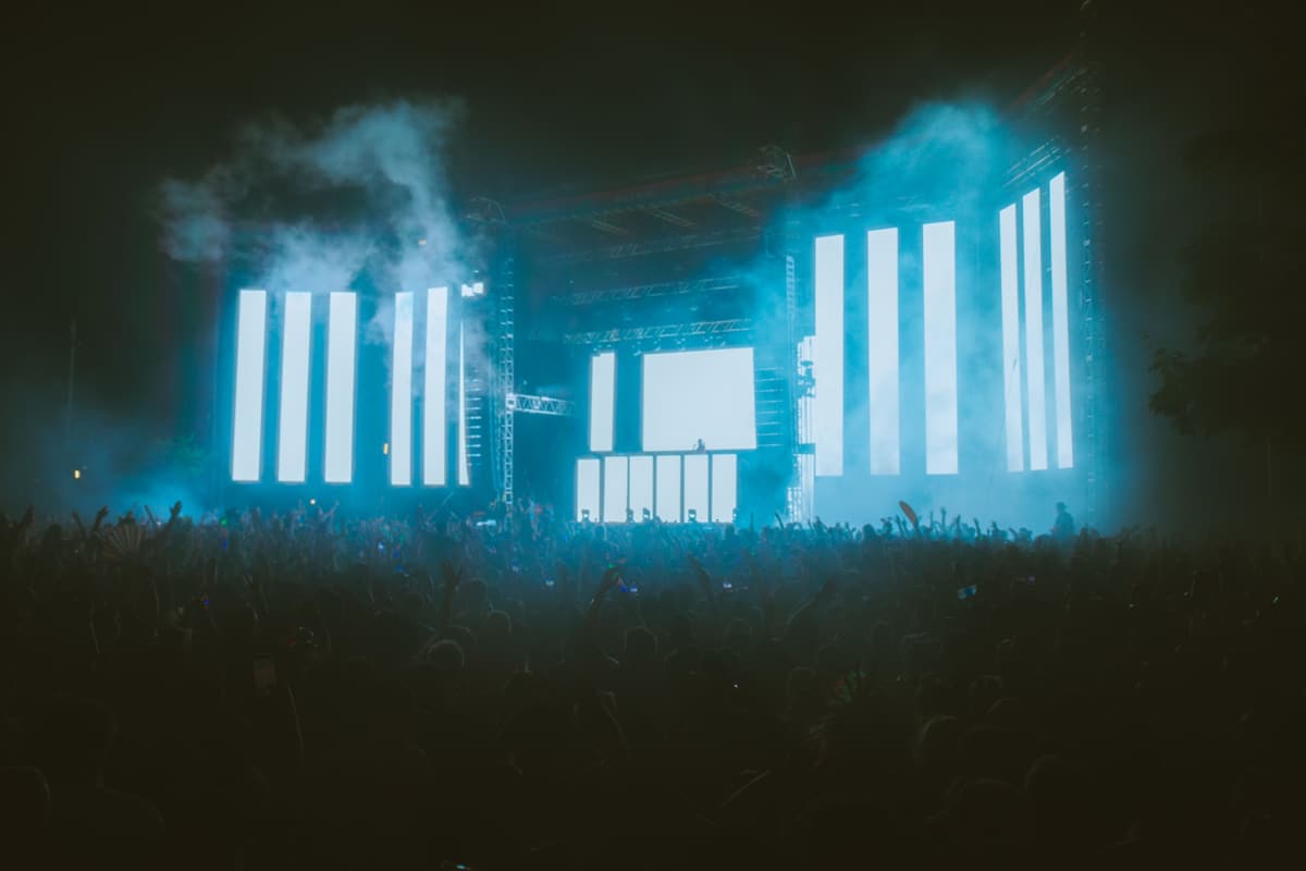 Open-Air-Bühne bei Nacht mit mehreren hochkant stehenden, hell leuchtenden LED-Flächen, Nebel und großem Publikum
