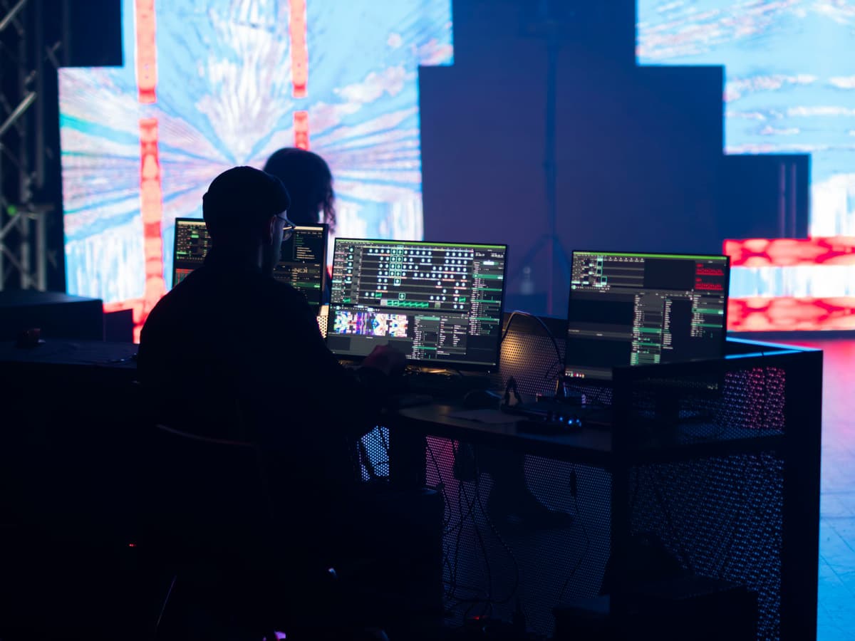 Techniker an einem Arbeitsplatz mit mehreren Monitoren, im Hintergrund eine LED-Wand mit farbigen Inhalten